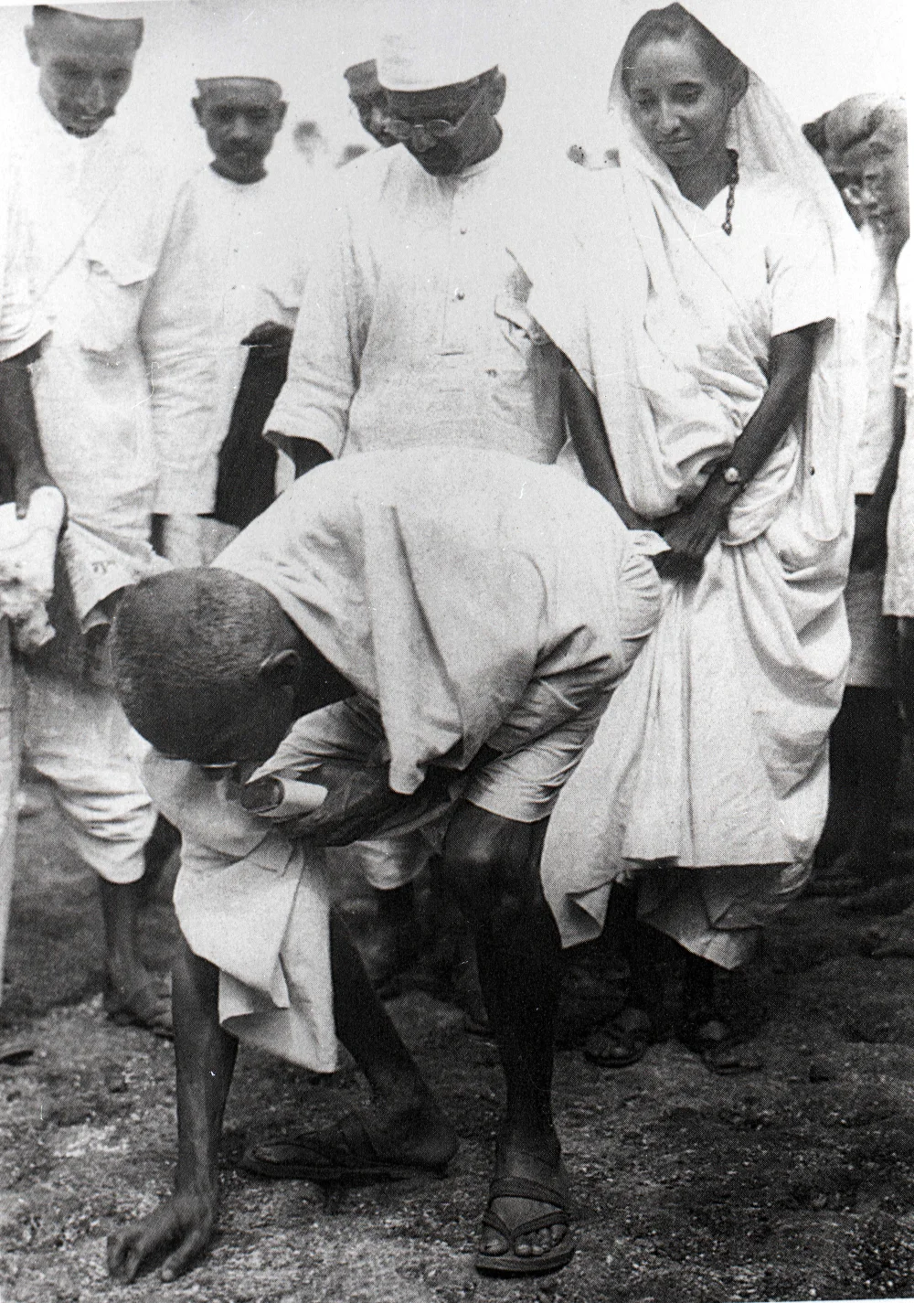 Gandhi, Tuz Yürüyüşü'nün sonunda Dandi sahilinde tuz toplarken; arkasında oğlu Manilal Gandhi ve Mithuben Petit görülüyor.
